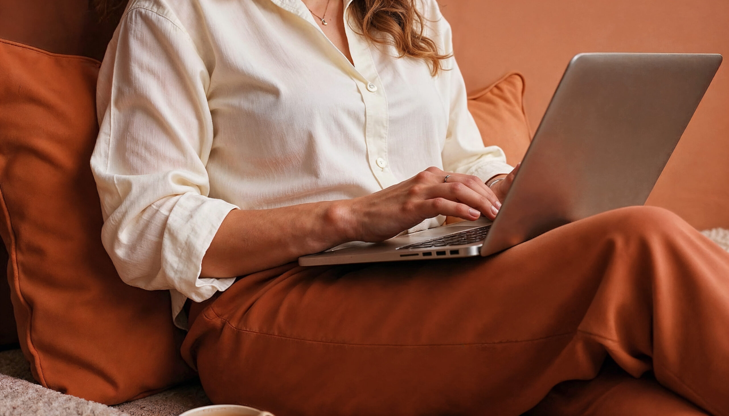 Woman sitting with a laptop on a couch in a cozy setting donna-seduta-con-un-portatile-su-un-divano-un-ambiente-accogliente